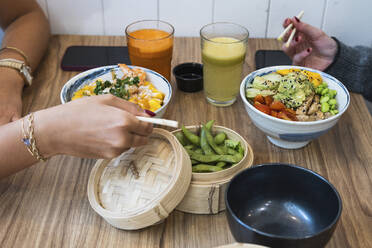 Weibliche Freunde essen chinesisches Essen mit Edamame-Bohnen im Korb im Restaurant - PNAF01679