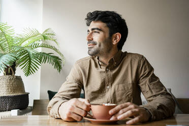 Smiling man with coffee cup sitting in restaurant - RCPF01101