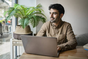 Lächelnder junger Geschäftsmann mit Laptop im Restaurant - RCPF01103