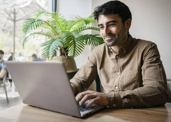 Smiling male entrepreneur using laptop at cafe - RCPF01107