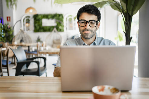 Junger männlicher Freiberufler mit Laptop am Tisch in einem Cafe - RCPF01109