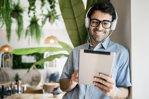 Männlicher Freiberufler lächelt, während er ein digitales Tablet in einem Café benutzt - RCPF01114