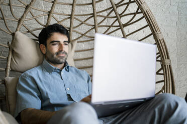 Male freelancer using laptop while sitting on chair swing in cafe - RCPF01115