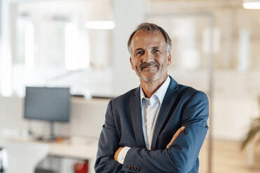 Male professional smiling while standing with arms crossed in office - GUSF05766