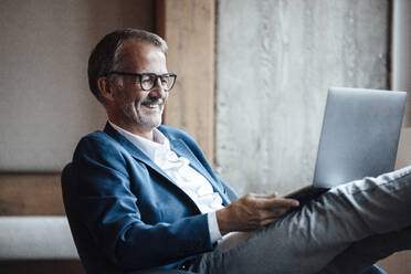 Smiling senior businessman working on laptop at office - GUSF05767