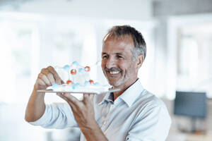 Businessman looking at molecule model over digital tablet in office - GUSF05769