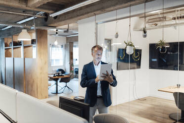 Senior male entrepreneur using digital tablet while standing in office - GUSF05773
