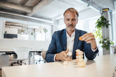 Male entrepreneur balancing wooden rock on table in office - GUSF05779