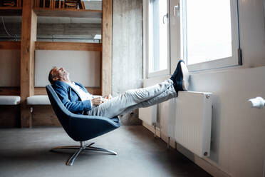 Glücklicher Geschäftsmann, der auf einem Stuhl im Büro sitzt und sich entspannt - GUSF05783