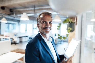 Smiling male entrepreneur holding digital tablet at office - GUSF05796