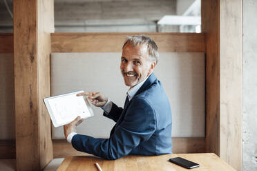 Lächelnder Geschäftsmann zeigt Geschäftsplan auf digitalem Tablet im Büro - GUSF05811
