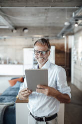 Male professional using digital tablet while standing at office - GUSF05822