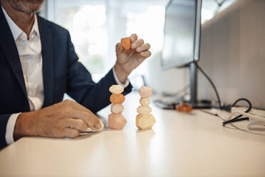 Senior businessman balancing wooden rock on table in office - GUSF05824