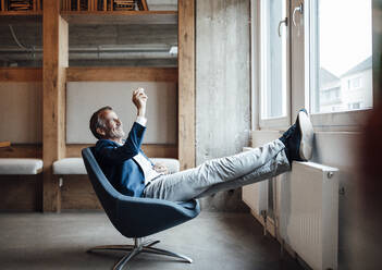 Businessman looking at wooden rock while sitting on chair at office - GUSF05831