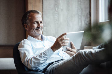 Businessman smiling while using digital tablet in office - GUSF05836