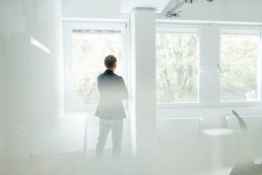 Businessman looking through window while standing at office - GUSF05845