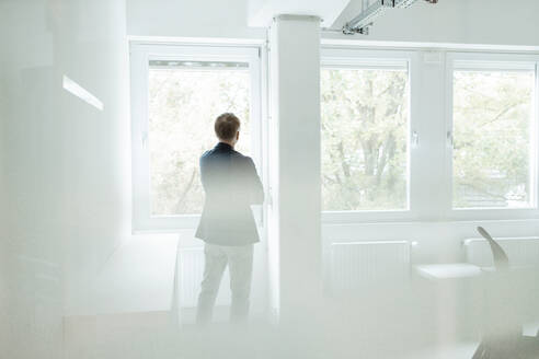 Geschäftsmann schaut durch ein Fenster, während er im Büro steht - GUSF05845