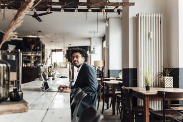 Reifer Geschäftsmann mit Laptop bei der Arbeit im Café - GUSF05856