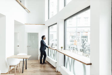 Mature male professional looking through window while standing by desk in office - GUSF05861