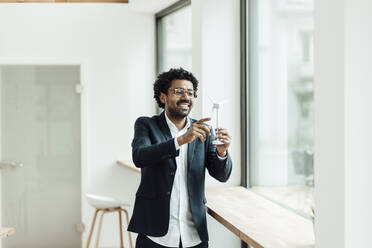 Smile male professional examining wind turbine model while standing in office - GUSF05879