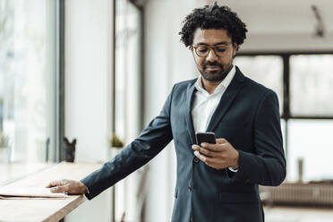 Businessman with curly hair using mobile phone in office - GUSF05889