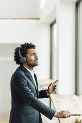 Male professional enjoying music listening through wireless headphones in office - GUSF05895