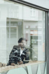 Male entrepreneur with smart phone in office seen through glass - GUSF05897