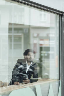 Männlicher Unternehmer mit Smartphone im Büro durch Glas gesehen - GUSF05897