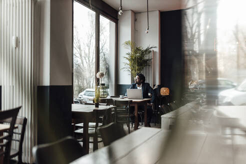 Älterer Geschäftsmann mit Laptop sitzt im Café und schaut durch das Fenster - GUSF05918