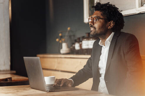 Männlicher Unternehmer mit Laptop am Tisch im Café sitzend - GUSF05932