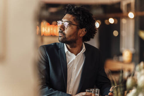 Männlicher Unternehmer mit Brille in einem Cafe, der wegschaut - GUSF05939