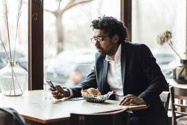 Geschäftsmann benutzt sein Smartphone beim Mittagessen im Restaurant - GUSF05942