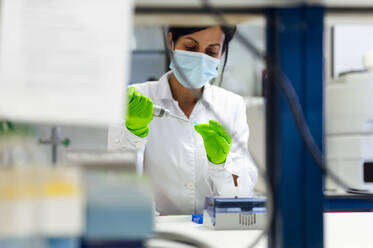 Weiblicher medizinischer Experte bei der Verwendung einer Pipette während eines Tests im Labor während einer Pandemie - PGF00578