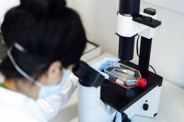 Mature female medical expert looking through microscope while analyzing medical samples in laboratory - PGF00585