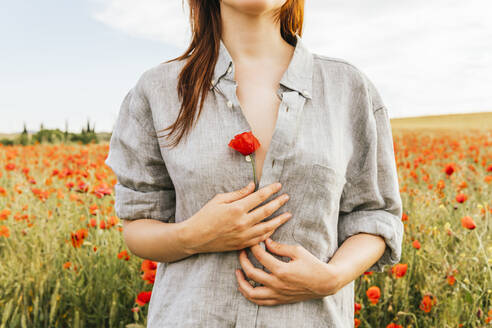 Frau mit roter Mohnblume in der Hand auf einem Feld stehend - MGRF00245