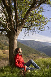 Mann lehnt sich an einen Baum und entspannt sich auf einem Berg - VEGF04556