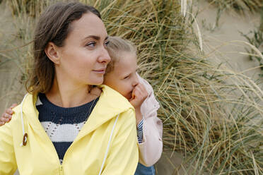 Mother and daughter looking away while spending leisure time at beach - OGF01044