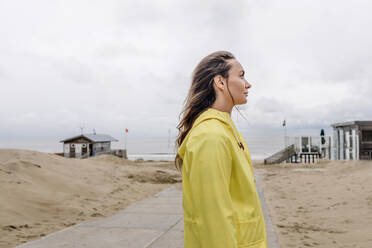 Frau in gelbem Regenmantel steht am Strand - OGF01048