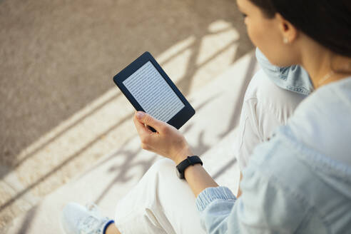 Woman reading an e-book while sitting on steps - OYF00373
