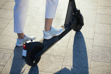 Woman riding electric scooter on footpath - OYF00379