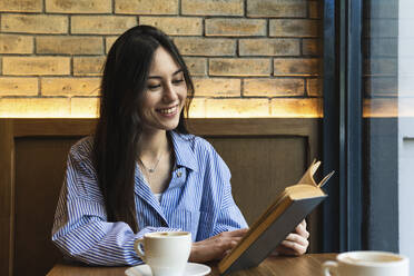 Woman with long hair reading book while sitting in bar - PNAF01686