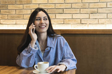 Junge Frau schaut weg, während sie in einer Bar mit ihrem Handy telefoniert - PNAF01687