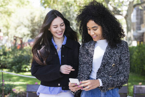 Multiethnische Freundinnen benutzen ihr Smartphone in einem öffentlichen Park - PNAF01690