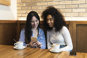 Freundinnen trinken Kaffee und benutzen ihr Smartphone in einer Bar - PNAF01691