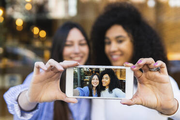 Female friends showing self portrait in smart phone - PNAF01698
