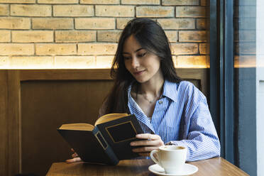 Beautiful woman reading book while having coffee at bar - PNAF01699