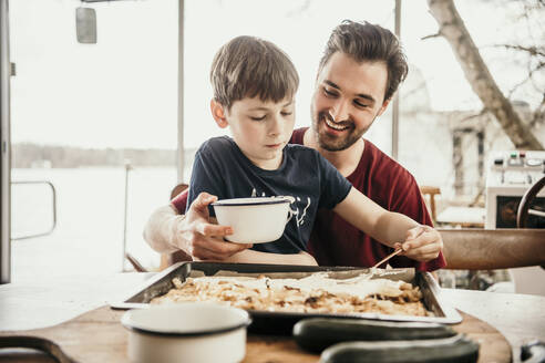 Smiling father assisting son in preparing food at houseboat - MJRF00574