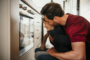 Vater und Sohn schauen beim Backen in den Ofen - MJRF00575