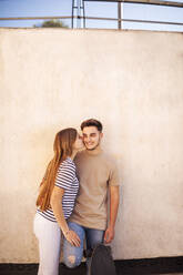 Girlfriend kissing on cheek of boyfriend cheek in front of wall - GRCF00720