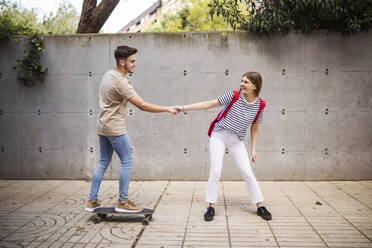 Boyfriend holding hand of girlfriend while skateboarding on footpath - GRCF00721